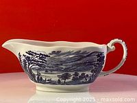 Blue and white ceramic gravy boat photographed from the side showing exterior scenery design