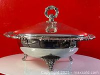 Silver plate footed bowl with lid, showing front and side profile to highlight decorative feet, ornate handle, and engraved lid design.