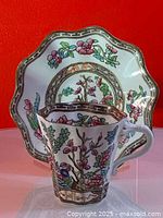 Front angled view of teacup sitting inside the matching scalloped saucer decorated with colorful Indian Tree floral patterns with gold trim.