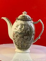 Front side view of the ceramic coffee pot showing the spout and rural village design.