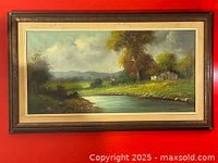 Framed early 20th century styled cottage landscape painting in dark wood frame on red wall.