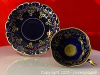 Front view of cobalt blue saucer with gold floral decorations alongside matching cup showing gold handle and inner gold details