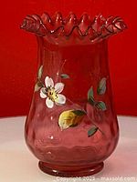 Front view of cranberry art glass vase with hand painted white flower and green leaves.