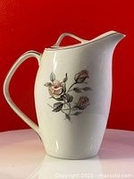 Front side view of the white ceramic coffee pot showing the floral hand painted design and curved handle