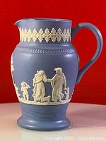 Blue jasperware style ceramic pitcher jug 6 inches high showing the decorative white relief classical figures on a blue matte body, detailed close-up of the front.