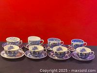 Photo of all eight blue and white cups each paired with its matching saucer on a black surface with red background.