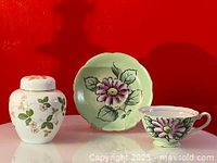 Photo of Wedgwood sugar bowl with lid alongside Japan occupied hand-painted floral teacup and saucer against a red background.
