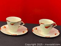 Two Myott hand painted 1930s Art Deco style teacups with triangular handles on decorated saucers, front view against red background.