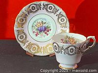 Teacup and saucer front view showing fruit and floral pattern with gold detailing on white porcelain