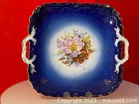 Full view of square shaped cobalt blue handled cake plate with hand-painted floral bouquet in center and gold rim accents.