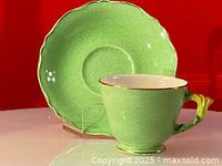 Green Royal Winton teacup and saucer displayed against red background, showing overall shape and crackle glaze finish.