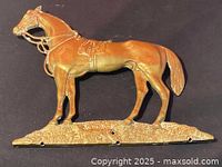 Front view of the solid brass horse wall hanging showing detailed horse figure, saddle, bridle, and base with mounting holes.