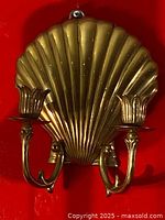 Front view of brass shell wall sconce with two candleholder arms against red background.