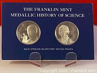 Front view of two silver proof medals set in blue Franklin Mint holder labeled 'The Franklin Mint Medallic History of Science Solid Sterling Silver/First Edition Proofs'