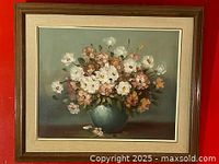 Full framed painting showing floral still life with multi-colored flowers in a blue vase, framed in a wooden frame with fabric inner border.