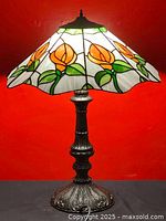 Full view of Tiffany style table lamp with stained glass shade featuring orange flowers and green leaves. Brass finish ornate metal base visible.