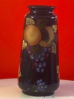 Front and side view of vintage ceramic vase with hand-painted fruit including apples, grapes, leaves on dark background