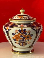Full view of vintage Imari ginger jar showing front floral design and hexagonal shape in orange, blue, and gold.