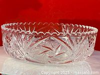 Side angle view showing cut starburst and geometric patterns on vintage crystal bowl against red background