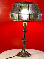 Photo showing full lamp with stained glass shade and brass base on white circular surface against red background.