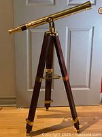 Front-left angled view showing full brass telescope and wooden tripod with brass fittings on hardwood floor.
