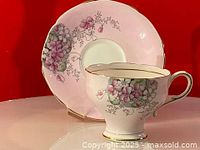 Teacup and saucer displayed together showing violet pink flower design and gold trim.