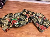 Four reversible outdoor chair cushions displayed on wood floor, showing both floral and striped patterns.