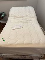 Full view of the white adjustable single bed with slightly raised head section, including a quilted bed cover and some paperwork on the mattress.