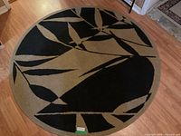 Photo showing the round carpet on hardwood floor with black and beige leaf design.