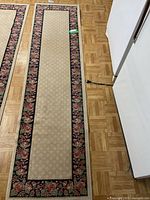 Full view of one beige carpet runner with floral border design placed on wood floor.