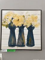 Frontal view of framed floral canvas painting showing yellow flowers in blue vases against white shiplap background.