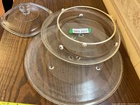 Three microwave oven glass turntables stacked and a glass lid with knob handle, showing size comparison and condition.