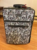 Front view of Buxton upright rolling luggage with floral tapestry pattern, front zipper pocket, and handle.