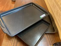 Photo showing three black metal cookie baking sheets stacked, highlighting their size and handles.