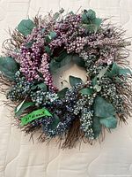 Full view of the wreath showing intertwined twig base with multicolored artificial berries and green leaves.