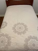 Full view of the double size quilt spread on a bed showing cream/beige background with brown floral mandala design.