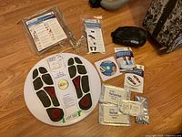 Top-down view of the Circulation Promoter device with attached cables laid out, instruction manuals, replacement electrode pads, and carrying cases.