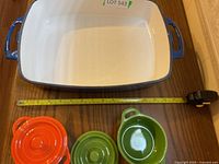 Large rectangular blue enamel over cast iron dish shown with measuring tape for size reference on wooden table.
