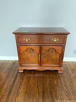 Full front view of the wooden buffet/server cabinet showing drawer with brass handles and double doors with carved shell motifs.