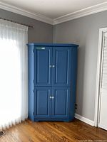 Blue painted corner wall unit with closed doors in a room with light hardwood floors and gray walls.