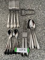 Five forks, four knives, four tablespoons, two teaspoons, and a metal vegetable peeler arranged on a countertop.