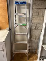 Full view of 6-foot aluminum step ladder against wall with silver frame and blue top step platform.