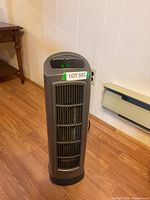 Full view of gray and black Lasco rotating space heater standing on wooden floor near white wall.