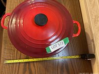 Top view of red Le Creuset Dutch oven with black knob on lid and tape measure showing approximately 28 cm diameter.