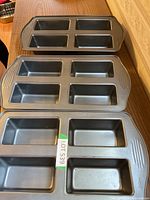 Three Wilton mini loaf pans laid out on a wooden table showing four rectangular molds per pan.
