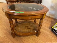 Round wooden occasional table with beveled glass top and wicker shelf as seen from above and side angles, showing table design and condition.