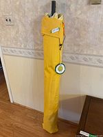 Yellow outdoor patio umbrella stored in yellow protective sleeve, with 'Lot 578' label attached, standing upright inside a room.
