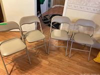 Set of 4 beige metal folding chairs arranged on wooden floor.