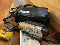 Photo showing Sony Handycam camcorder with black leather carrying case and manual, also includes shoulder strap.