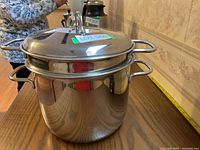 Photo displaying the large stainless steel stockpot and the steamer insert stacked together, showing the reflective shine and loop handles on each side.